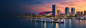 Yas Marina at dusk with yachts, waterfront towers and a lit lattice-roofed building
